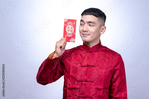 An Asian man in a red traditional Chinese Tang suit smiles while holding and presenting a single red envelope, symbolizing prosperity, isolated against a plain white background. photo