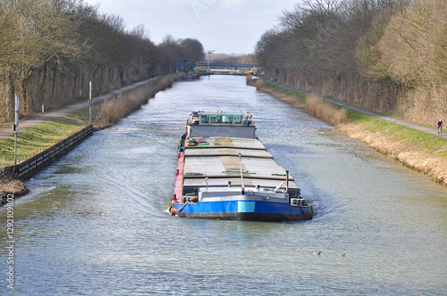 A barge sails through a calm canal in Germany. Loaded or empty, it is clearly on its way, symbolizing movement and logistics on Europe’s waterways.
