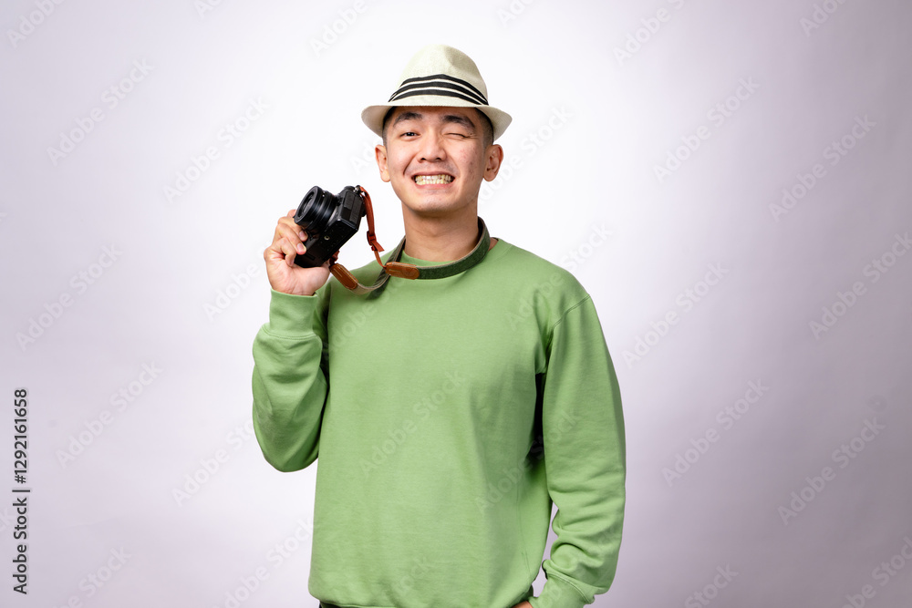 An Asian man wearing a fedora hat and a green sweater is holding a camera while smiling. The camera strap hangs around his neck, traveler photographer vibe against a white background An Asian man wearing a fedora hat and a green sweater is holding a camera while smiling. The camera strap hangs around his neck, traveler photographer vibe against a white background