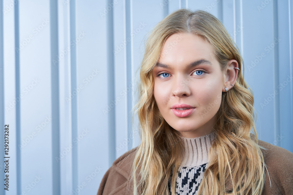 Blonde woman with light blue eyes posing confidently against a metallic background Blonde woman with light blue eyes posing confidently against a metallic background