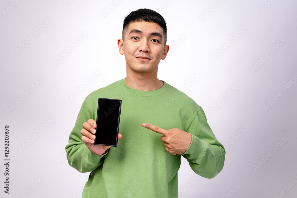 An Asian man in a green sweatshirt is smiling and pointing at a smartphone with a blank screen. He holds the phone in one hand while gesturing towards it with excitement. The background is white An Asian man in a green sweatshirt is smiling and pointing at a smartphone with a blank screen. He holds the phone in one hand while gesturing towards it with excitement. The background is white