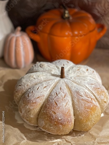 A beautifully crafted pumpkin shaped sourdough bread, dusted in flour, sits on a rustic table with autumn-themed decor. Perfect for Thanksgiving or fall celebrations, embodying cozy and festive vibes.