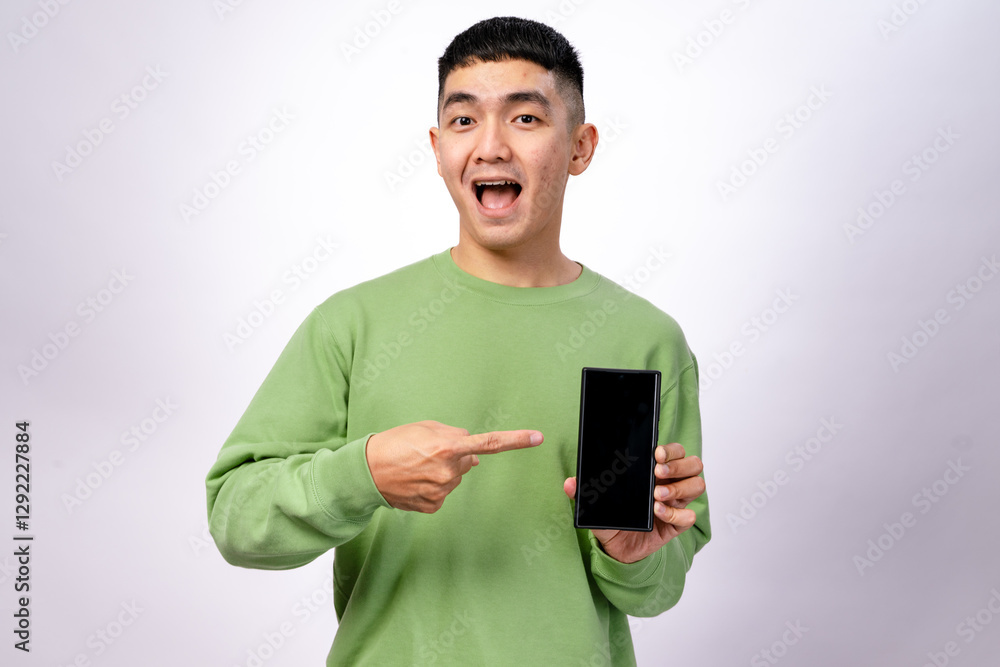 An Asian man in a green sweatshirt is smiling and pointing at a smartphone with a blank screen. He holds the phone in one hand while gesturing towards it with excitement. The background is white An Asian man in a green sweatshirt is smiling and pointing at a smartphone with a blank screen. He holds the phone in one hand while gesturing towards it with excitement. The background is white