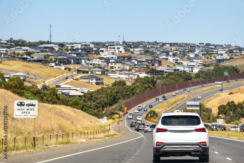 A multi-lane, busy highway or main road with many cars, alongside a hillside residential development near Geelong, Australia, with many houses. concept of a new estate, suburban expansion