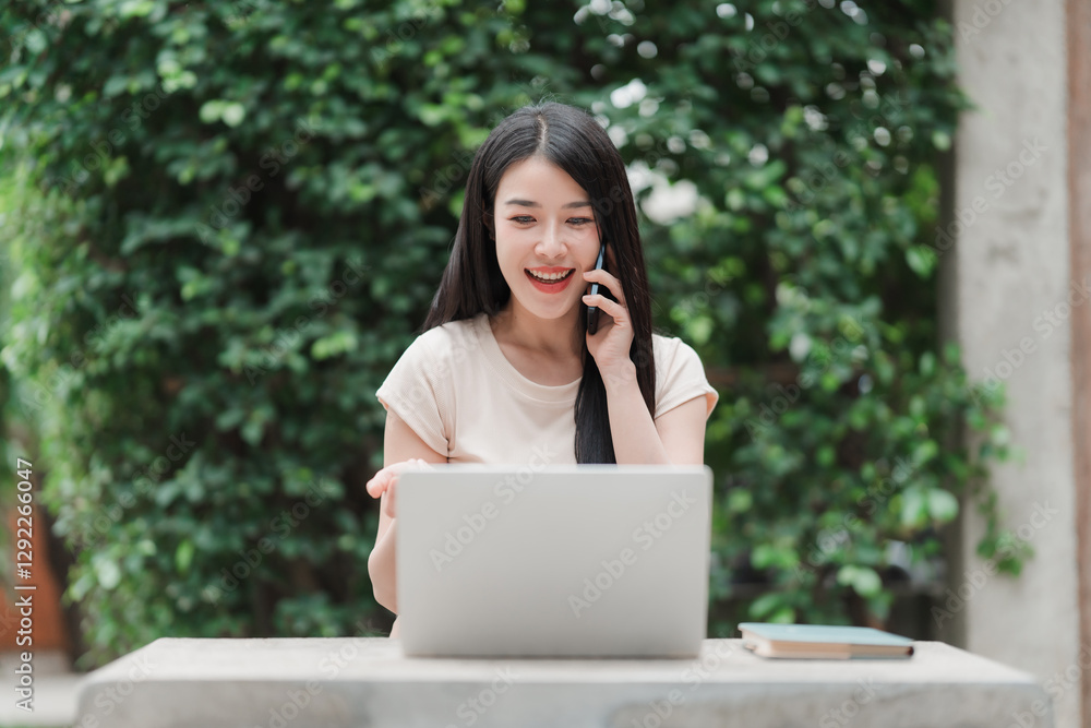 Communicating with Nature: A young, Asian woman with a radiant smile engages in a phone conversation, while working on her laptop amidst lush greenery. Communicating with Nature: A young, Asian woman with a radiant smile engages in a phone conversation, while working on her laptop amidst lush greenery.