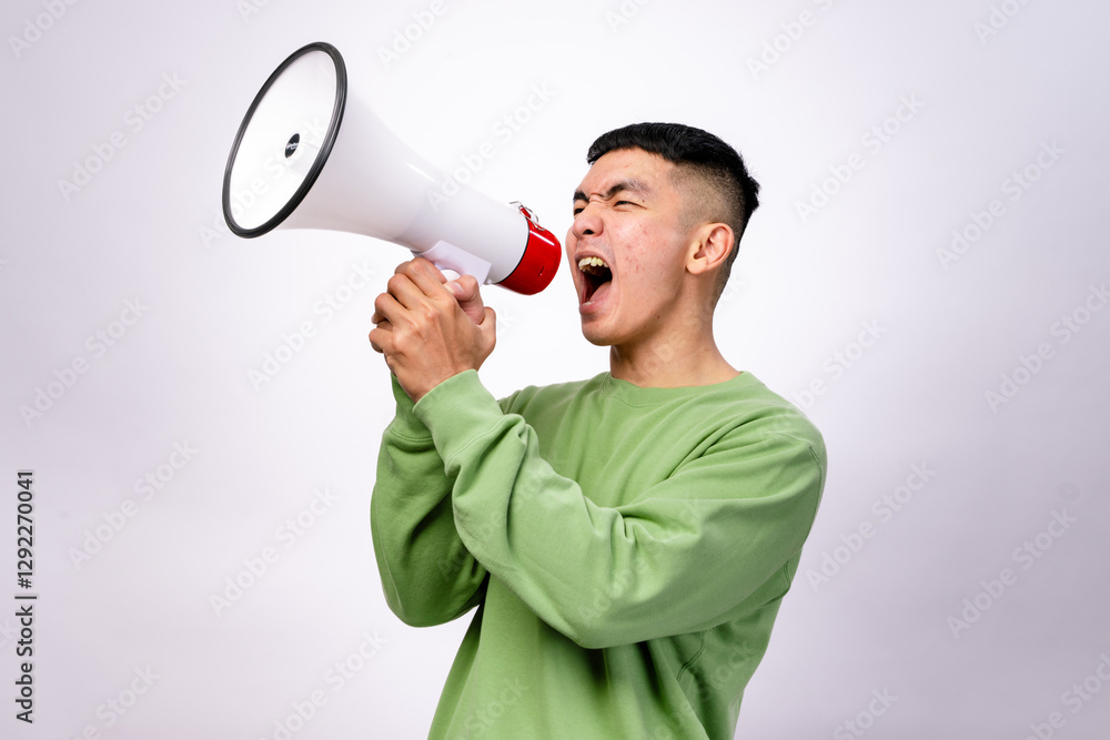 An Asian man in a green sweatshirt is shouting into a white megaphone with a red handle. He looks intense and expressive. The background is plain white An Asian man in a green sweatshirt is shouting into a white megaphone with a red handle. He looks intense and expressive. The background is plain white