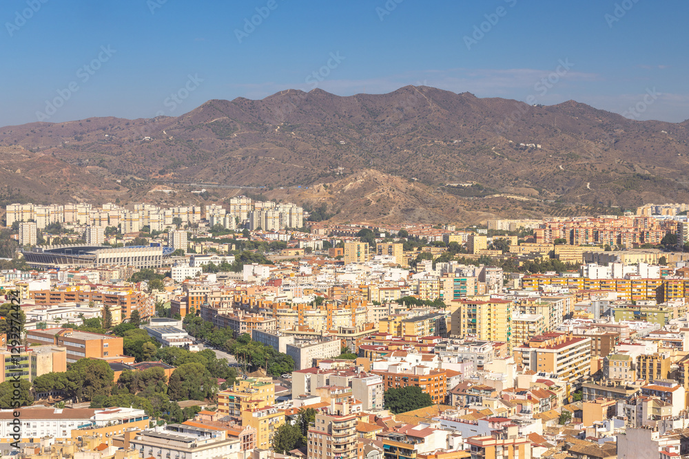 Malaga, seaside city in Andalusia, Spain, Europe. Panoramic city view with mountains in the background. Residential buildings and a stadium are visible. Malaga, seaside city in Andalusia, Spain, Europe. Panoramic city view with mountains in the background. Residential buildings and a stadium are visible.