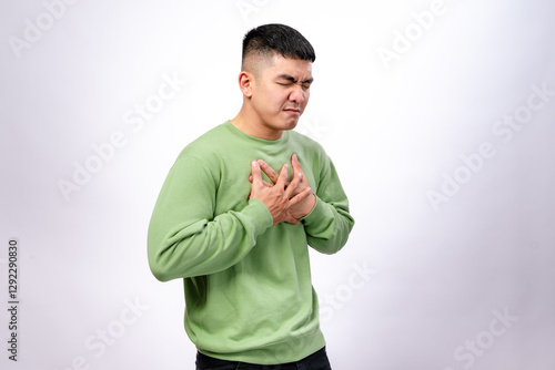 An Asian man in a green sweatshirt clutches his chest with both hands, his face showing discomfort and pain. He appears to be experiencing chest pain or distress. The background is plain white