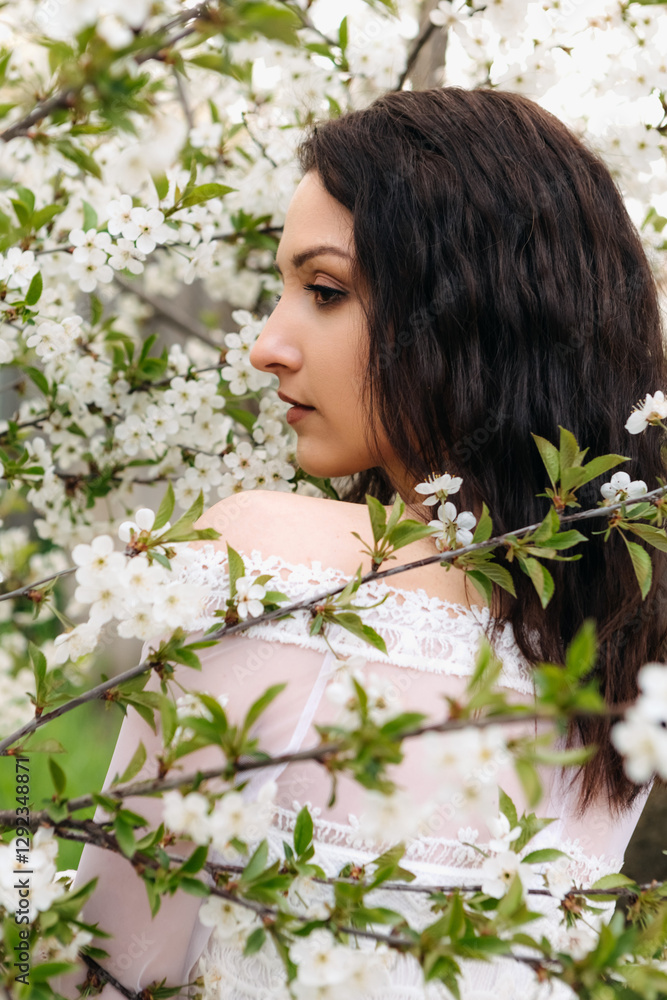 Brunette female in flowing white dress standing amid cherry blossoms, experiencing serene spring garden landscape with soft floral background Brunette female in flowing white dress standing amid cherry blossoms, experiencing serene spring garden landscape with soft floral background