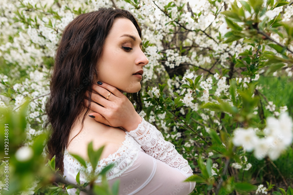 Attractive young woman with long dark hair and elegant white dress posing in a blooming garden, enjoying the fresh air and the beauty of nature during springtime Attractive young woman with long dark hair and elegant white dress posing in a blooming garden, enjoying the fresh air and the beauty of nature during springtime