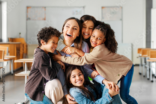 Friendly atmosphere in the classroom, happy diverse kids embracing female teacher appreciating and thanking educator at the end of year