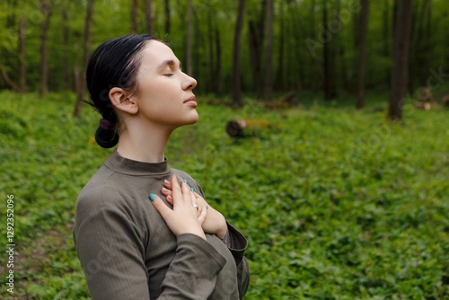 Young woman practicing mindfulness in a peaceful forest, taking a deep breath with closed eyes and hands on her chest, surrounded by lush greenery and tranquility