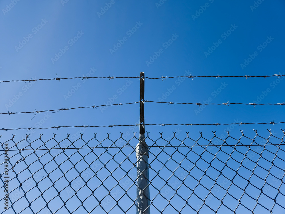 Barbed wire chain link fence against a blue sky Barbed wire chain link fence against a blue sky