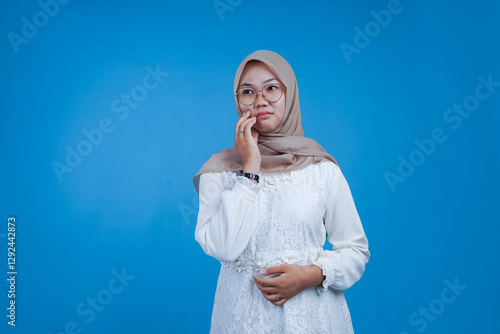 Young Woman in Hijab with Thoughtful Expression, Hand on Chin, on Blue Background