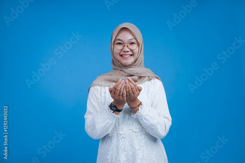 Happy Young Woman in Hijab Holding Hands Together in Front of Blue Background