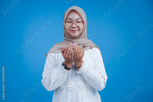 Happy Young Woman in Hijab Holding Hands Together in Front of Blue Background
