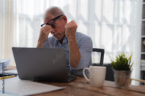 Fotografia Senior businessman is having a headache and feeling tired from working on a lapt