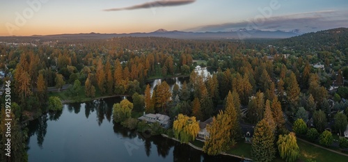 Fototapeta Naklejka Na Ścianę i Meble -  Aerial view of a serene lake nestled within a Drake Park, surrounded by lush greenery and mountains in the background. Evening light bathes the scene. River West, Bend, Oregon, United States