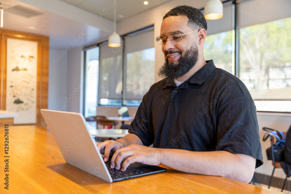 A joyful African American man is typing on his laptop at a beautifully crafted wooden table in an inviting workspace, enjoying a creative and focused environment perfect for teamwork and growth A joyful African American man is typing on his laptop at a beautifully crafted wooden table in an inviting workspace, enjoying a creative and focused environment perfect for teamwork and growth