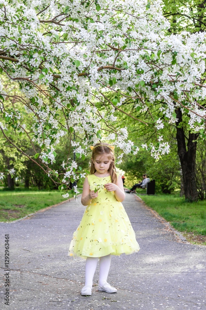 Little girl in yellow dress standing under blossoming apple tree and looking at the flowers. Little girl in yellow dress standing under blossoming apple tree and looking at the flowers.