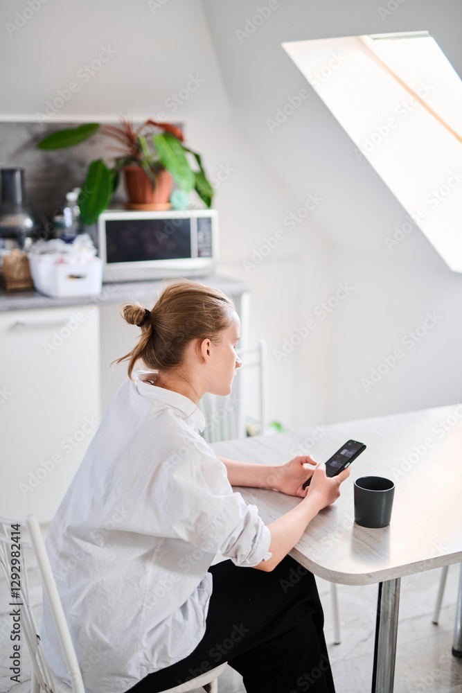 Cute teenage schoolgirl drinks coffee for breakfast and checks email, looks at smartphone screen Cute teenage schoolgirl drinks coffee for breakfast and checks email, looks at smartphone screen