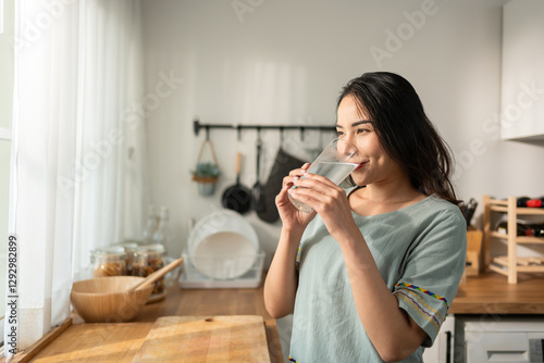 Asian young attractive woman drink a glass of water in kitchen at home. 