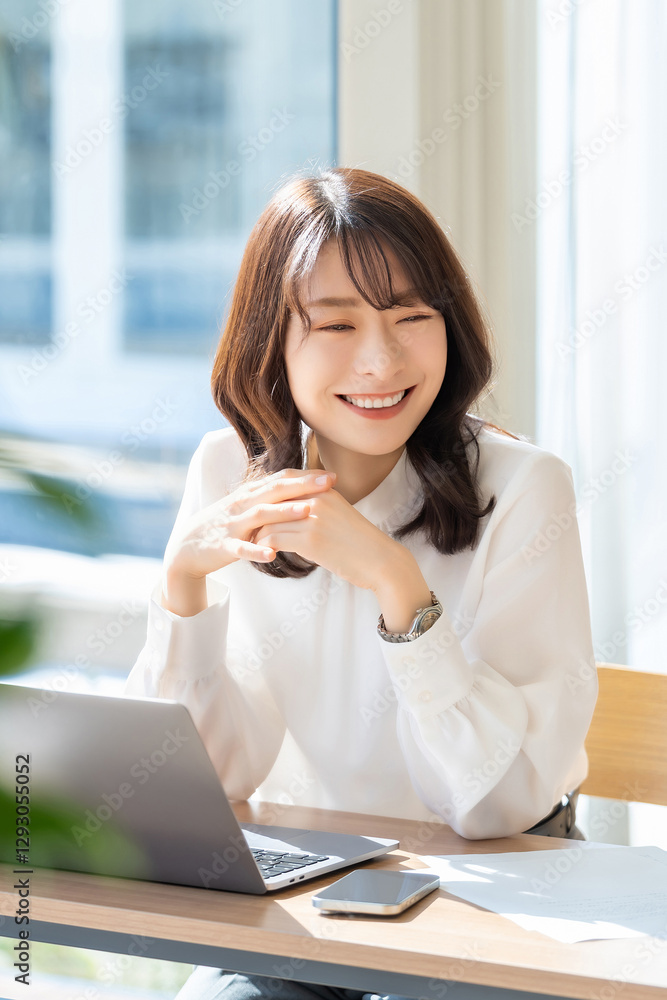 春の光が差し込むオフィスでデスクワークをする笑顔の女性・ビジネスウーマン 春の光が差し込むオフィスでデスクワークをする笑顔の女性・ビジネスウーマン