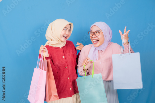 Two women are holding shopping bags and a credit card, smiling and posing for a photo. Scene is happy and celebratory, as the women are excited about their shopping haul