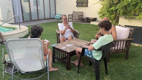 Family playing cards together in their backyard garden on a warm summer afternoon, enjoying quality time outdoors while relaxing and bonding in a peaceful and cheerful environment in Spain