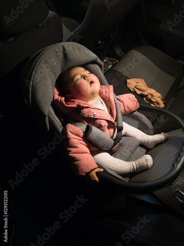 Adorable sleeping baby sitting in an infant car seat placed rear facing in the back seat of a car. at night with dim light. high-angle shot