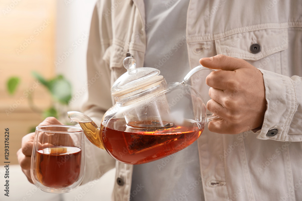 Young man pouring tea into glass cup at home, closeup Young man pouring tea into glass cup at home, closeup