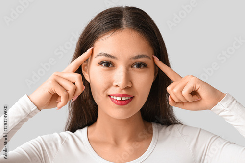 Wallpaper Mural Young Asian woman pointing at her head on grey background. Brain Injury Awareness Month Torontodigital.ca