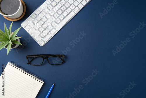 Workspace with keyboard, laptop, office supplies, pen, green leaf and coffee cup. Flat lay, top view blue office desk