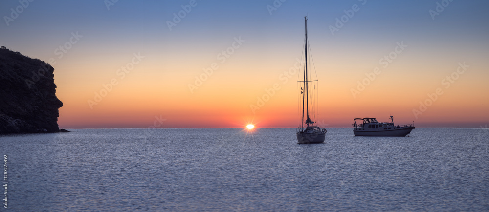 Breathtaking Sunrise Over Cala Joncols With Tranquil Boats in Costa Brava Waters, Roses, Catalonia Breathtaking Sunrise Over Cala Joncols With Tranquil Boats in Costa Brava Waters, Roses, Catalonia