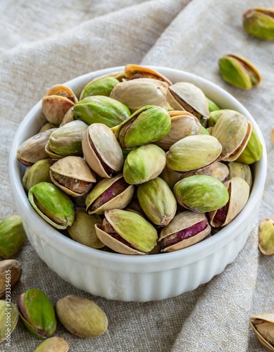 Pistachio Kernels, Roasted and Salted Nuts in a White Bowl on Linen Fabric – Shelled Pistacia Vera, Crunchy Toasted and Salted Snack, Close-Up from Above