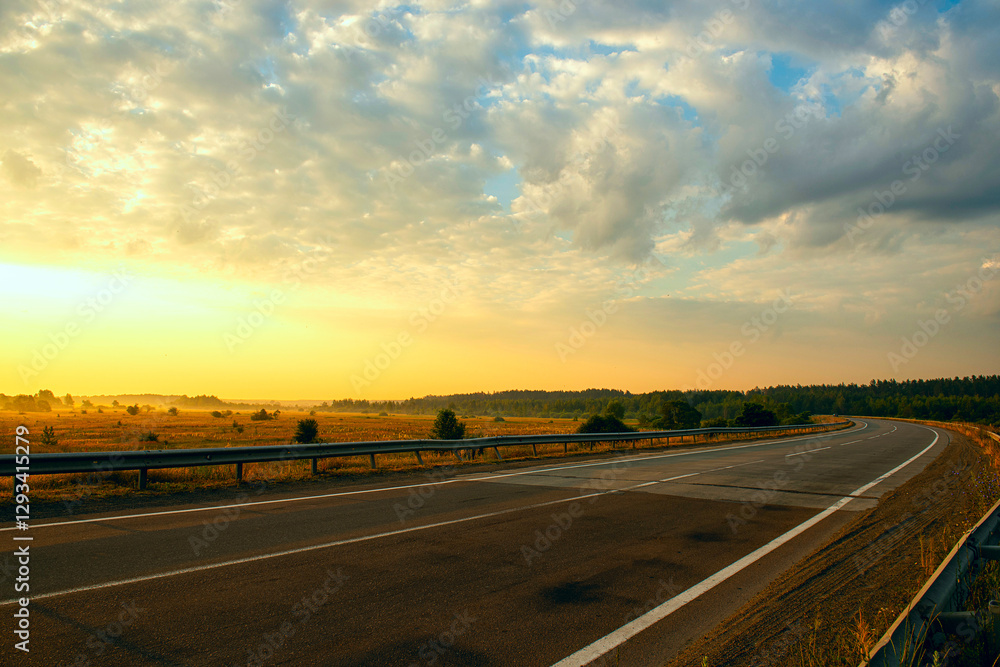Naklejka premium A deserted asphalt road going around the bend, at dawn among the fields. soft sunlight illuminates everything around.