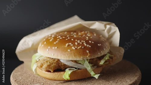 A delicious crispy chicken burger rotates on a dark background, showcasing its golden sesame seed bun, fresh lettuce, and crunchy fried chicken fillet. Close up shot