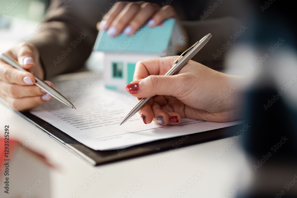 Client and real estate agent signing contract, holding pens and model house in modern office environment. Client and real estate agent signing contract, holding pens and model house in modern office environment.