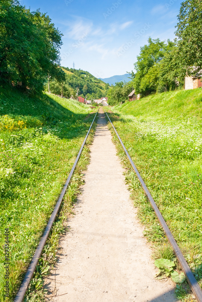 Obraz premium old railroad passes through the valley. mountainous countryside in morning light. sunny weather with blue sky and clouds. outdoor adventure in western ukraine