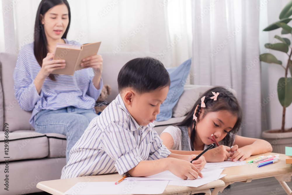 Asian mother reading book while two children focus on drawing. Boy and girl seated at small tables in living room. Cozy family time with mother supervising. Bright indoor setting, learning activities. Asian mother reading book while two children focus on drawing. Boy and girl seated at small tables in living room. Cozy family time with mother supervising. Bright indoor setting, learning activities.