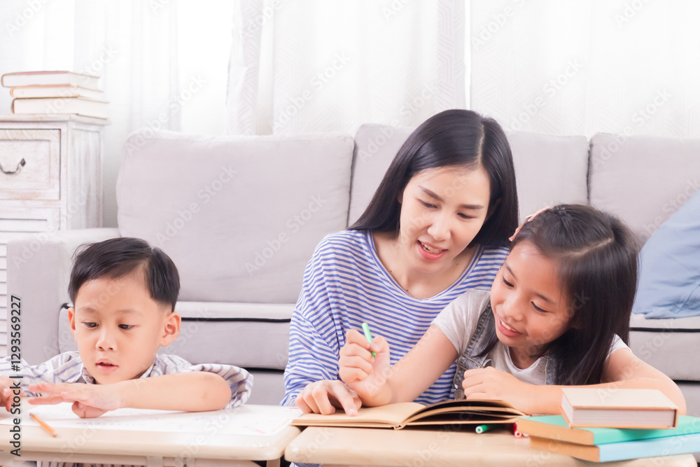 Asian beautiful mother helping two young children doing homework at home, boy and girl engaged in creative activity in cozy living room setting. Family bonding and education, spending time together. Asian beautiful mother helping two young children doing homework at home, boy and girl engaged in creative activity in cozy living room setting. Family bonding and education, spending time together.