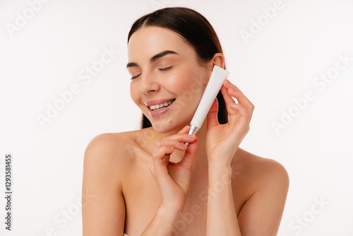 Portrait of smiling woman holding a skincare tube against a simple white background, expressing joy and beauty. Ideal representation of skincare, self-care, beauty routines, and wellness inspiration.