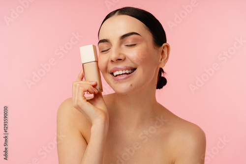 Joyful individual showcasing facial foundation while radiating confidence and beauty on a pink backdrop.