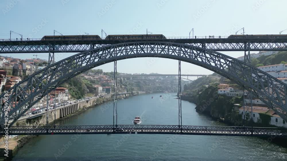 A drone shot of a train crossing the iconic Dom Luís I Bridge in Porto, Portugal, with a beautiful view of the Douro River below. A drone shot of a train crossing the iconic Dom Luís I Bridge in Porto, Portugal, with a beautiful view of the Douro River below.