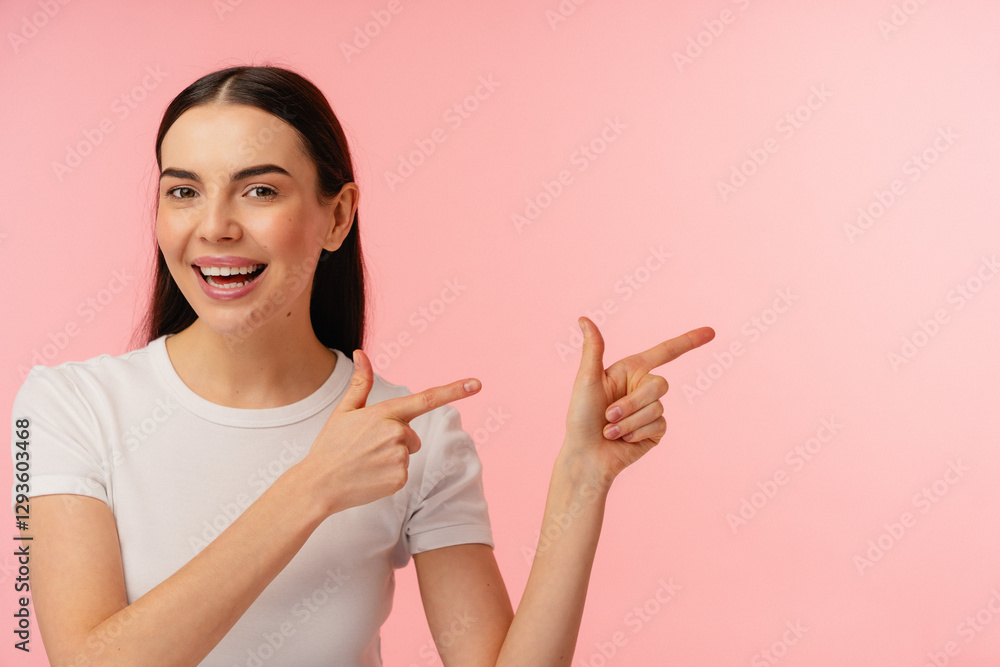 Portrait of an individual wearing a white shirt, smiling, and pointing with both hands. The background is a bright and cheerful pink color, adding positivity and energy to the overall composition. Portrait of an individual wearing a white shirt, smiling, and pointing with both hands. The background is a bright and cheerful pink color, adding positivity and energy to the overall composition.