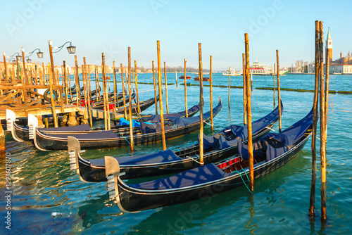 Elegant gondolas moored in Venice, Italy, with the turquoise waters of the Grand Canal reflecting sunlight. Wooden poles and historic architecture add charm to this classic Venetian scene