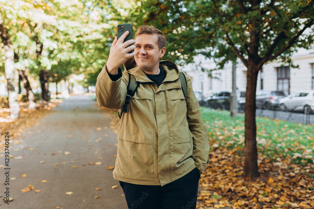 Smiling 30s man with backpack taking photo on park background. Selfie time. Holidays, rest, blogging banner. Charming male wearing stylish outfit have fine