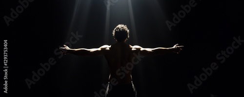 An image of a male athlete standing in a dark environment with arms outstretched under lighting. A muscular man prepares to perform stunts. Image for blogs about fitness, motivation, and sports themes