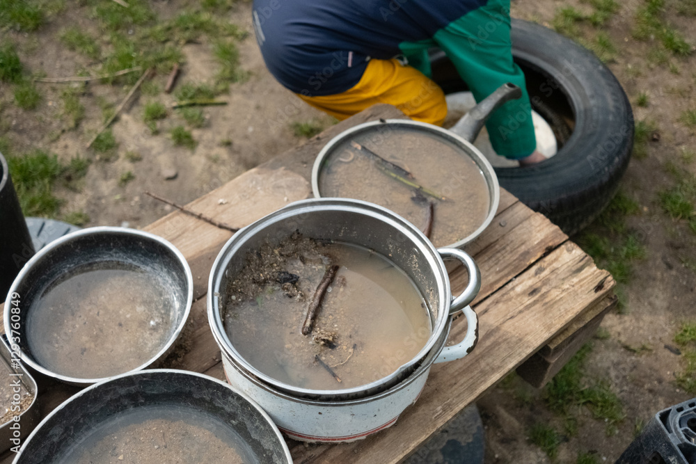 A lively mud kitchen in a kindergarten where children engage in free play, using pots, pans, and plates filled with sand, water, mud, and leaves. Montessori-inspired hands-on learning. A lively mud kitchen in a kindergarten where children engage in free play, using pots, pans, and plates filled with sand, water, mud, and leaves. Montessori-inspired hands-on learning.