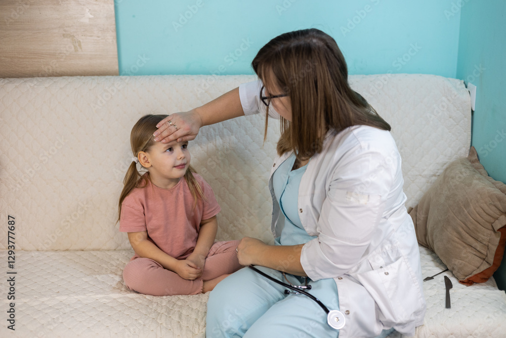 Fototapeta premium A sick child has a doctor called to her home. A female pediatrician visits the little girl at home and measures her temperature by placing her hand on her forehead while she sits on the couch.